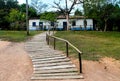 Path with a wooden railing and a rustic white house with trees in the background. Royalty Free Stock Photo
