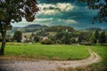 Pathway through a green field to the forest with sun rays coming behind the cloud sin the sky Royalty Free Stock Photo