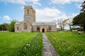 Pathway lined with yellow buttercups and daffodils leading to the Church of St Mary in the village of Burton Bradstock, Dorset, UK