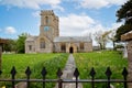 Pathway lined with yellow buttercups and daffodils leading to the Church of St Mary in the village of Burton Bradstock, Dorset, UK