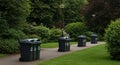 A pathway in a park is lined with several black recycling bins on wheels. Each bin Royalty Free Stock Photo