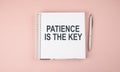 PATIENCE IS THE KEY text on notebook with pen on the pink background