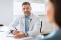 Patient-centered care. Cheerful male doctor consulting lady patient, filling form at consultation in clinic Royalty Free Stock Photo