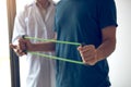 Patient doing stretching exercise with a flexible exercise band and a physical therapist hand to help in clinic room Royalty Free Stock Photo