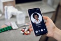 Patient hand holding smart phone and calling to female African doctor for online medical consultation. Focus on screen Royalty Free Stock Photo