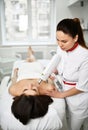 Patient lies on the couch while doctor performs a cosmetic procedure on her face with medical equipment. In a beauty shop