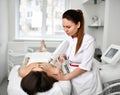 Patient lies on the couch while doctor performs a cosmetic procedure on her face with medical equipment. Equiped beauty shop