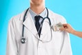 Patient putting bribe into doctor`s pocket on light blue background, closeup. Corruption in medicine Royalty Free Stock Photo