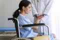 Young woman unwell sitting on wheelchair while doctor man standing beside holding her hands comforting and encouragement