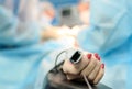 Patients hand with a sensor on the blurry background of the group of doctors in the operating room. Close up Royalty Free Stock Photo