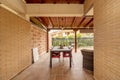 Patio of a detached house with light brown stoneware floors, exposed brick walls, lawned gardens and a porch made of varnished Royalty Free Stock Photo