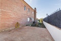 Patio of a detached house with light brown stoneware floors, exposed brick walls, lawned gardens and swings for children Royalty Free Stock Photo