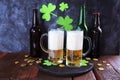 Patrick day, foamy beer in glass mugs and a bottle, gold coins on a wooden table, green shamrock on a dark background Royalty Free Stock Photo