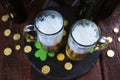 Patrick day, foamy beer in glass mugs and a bottle, gold coins on a wooden table, green shamrock on a dark background Royalty Free Stock Photo