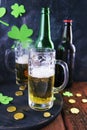 Patrick day, foamy beer in glass mugs and a bottle, gold coins on a wooden table, green shamrock on a dark background Royalty Free Stock Photo