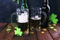 Patrick day, foamy beer in glass mugs and a bottle, gold coins on a wooden table, green shamrock on a dark background Royalty Free Stock Photo