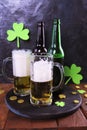 Patrick day, foamy beer in glass mugs and a bottle, gold coins on a wooden table, green shamrock on a dark background Royalty Free Stock Photo