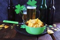 Patrick Day, foamy beer in glass mugs and a bottle, paprika chips, gold coins, on a red wooden table, a green shamrock Royalty Free Stock Photo