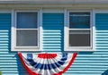 Patriotic bunting displayed beneath two wood windows on a blue painte house for Memorial Day or the 4th of July USA