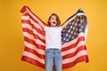 Happy child, cute girl with American flag on yellow studio background. USA celebrate July 4th, independence Day.