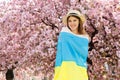 Patriotic Lady with Ukrainian Wrapped on Flag Smiling While Standing Outside near Sakura Blooming Trees. Proud of