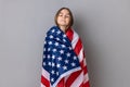 Patriotic little girl standing wrapped in american flag, keeping eyes closed, relocating to America. Royalty Free Stock Photo