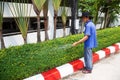 PATTAYA, THAILAND - MARCH 22, 2016: Thai Asian man gardener watering a green hedge. Red and white marking