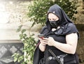 Woman in a fantasy costume with black face mask playing with her cell phone at a public fantasy festival Royalty Free Stock Photo