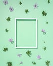 Pattern of beautiful purple flowers and leaves of wildflower with a white photo frame on a pastel green background. Flat lay