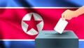 Male hand puts down a white sheet of paper with a mark as a symbol of a ballot paper against the background of the North Korea fla