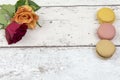 Multicoloured macaroons with roses on a white wooden background