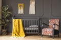 Patterned armchair next to bed with yellow blanket in kid`s bedr