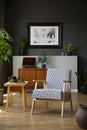 Patterned armchair next to wooden table in dark grey living room interior with poster. Real photo