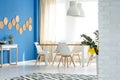 Patterned black and white carpet on the floor of neat dining room with wooden table and white chairs