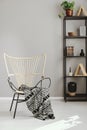 Patterned blanket on armchair in grey living room interior. Real photo