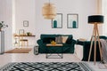 Patterned carpet and lamp in bright open space interior with posters above green settee. Real photo Royalty Free Stock Photo