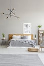 Patterned carpet and pouf in spacious grey bedroom interior with poster above wooden bed. Real photo