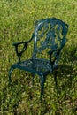 Patterned green metal chair stands on a green meadow on a sunny day