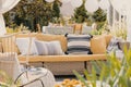 Patterned pillows on a wicker couch in a garden. Blurred close-up of a plant. Real photo