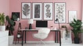 Patterned poster on table with computer monitor in Pink home office interior with plants Royalty Free Stock Photo