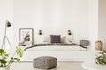 Patterned pouf in front of white bed in bright bedroom interior