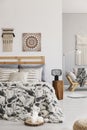 Patterned sheets on bed next to lamp on wooden stool in bedroom interior with poster