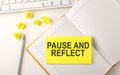 PAUSE AND REFLECT text on sticker on the diary with keyboard and pencil