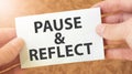 PAUSE AND REFLECT word inscription on white card paper sheet in hands of a businessman Royalty Free Stock Photo