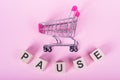 PAUSE - word on wooden cubes, on a pink background with a shopping trolley