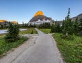 Paved foot path cuts through pine trees as it leads to a sunlit mountain peak.