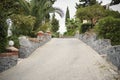 Paved pathway with palm trees and green bushes on both sides leading to the sea or park. Walking path