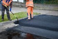 Paving workers adjust new layer of asphalt with shovels in reconstruction of road