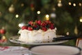 Pavlova with cream & berries, Australian dessert. In the background is the Christmas tree with fairy lights and baubles.