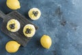 Pavlova dessert with lemon cream and blueberries on a wooden board with lemons on a blue background. Flat lay